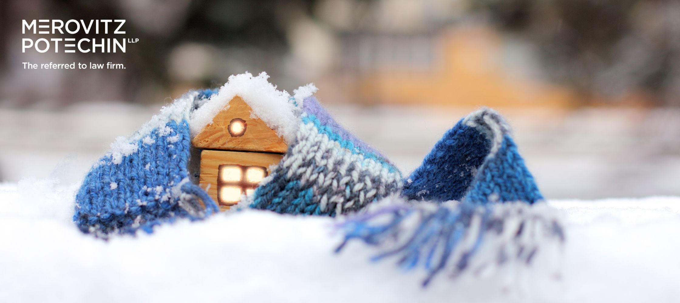 Buying a Home in Winter – A cozy wooden house wrapped in a warm blue knitted scarf, surrounded by fresh snow, symbolizing the importance of protecting your home during the colder months.